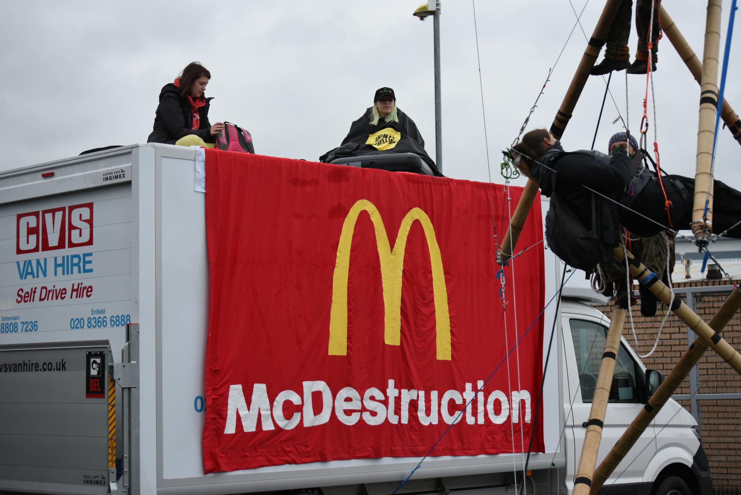 NO SALES Handout photo dated 22/05/21 issued by Animal Rebellion showing Animal Rebellion protesters suspended from a bamboo structure and on top of a van, being monitored by police officers, outside a McDonalds distribution site in Basingstoke,