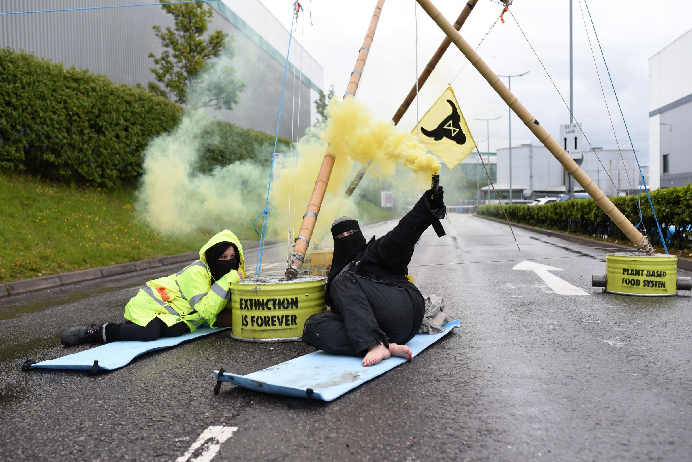 NO SALES Handout photo dated 22/05/21 issued by Animal Rebellion showing Animal Rebellion protesters attached to a bamboo structure and releasing a yellow smoke canister, outside a McDonalds distribution site in Basingstoke, Hampshire, which is being