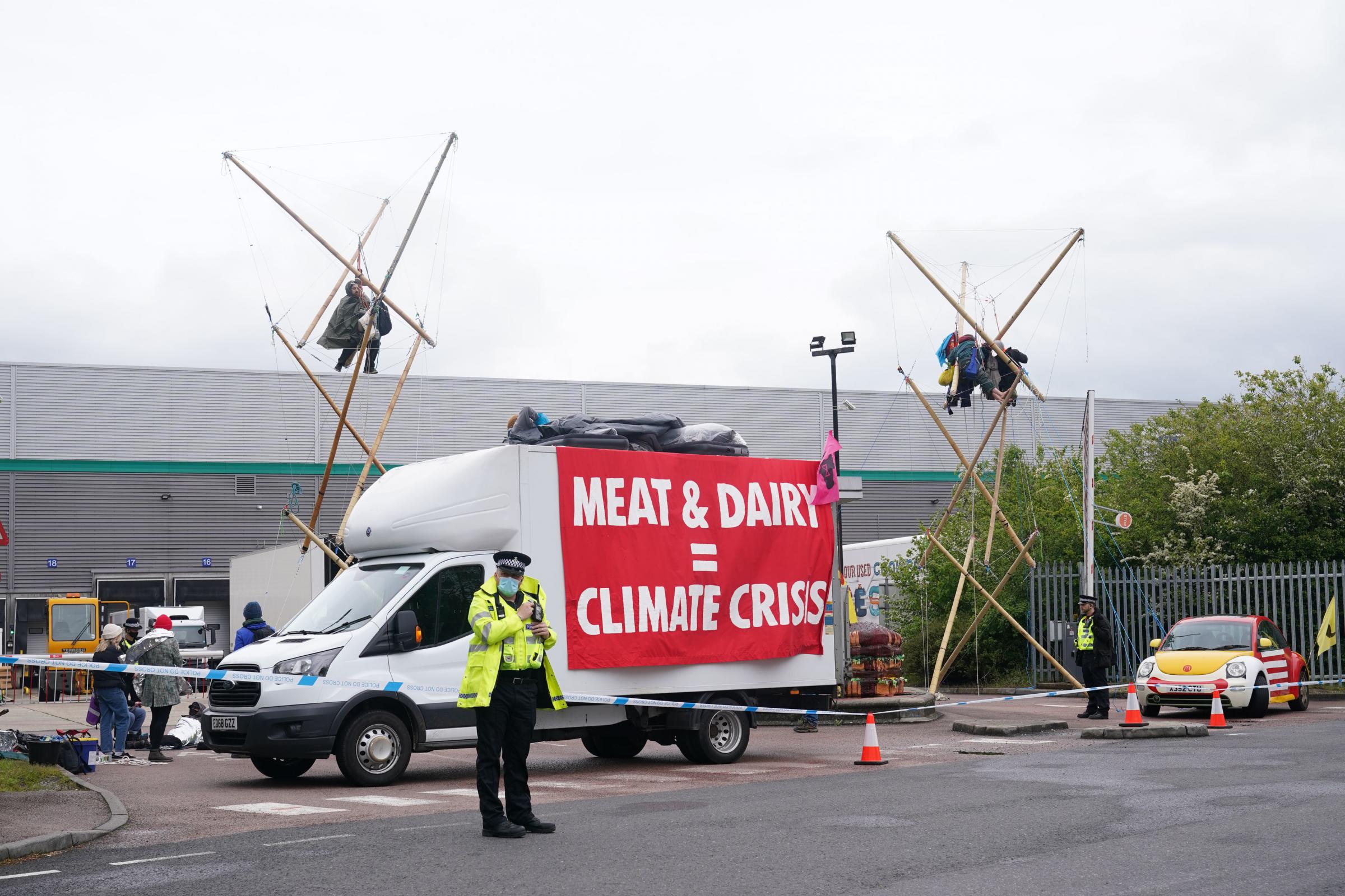 Animal Rebellion protesters suspended from a bamboo structure and on top of a van, being monitored by police officers outside a McDonalds distribution site in Hemel Hempstead, Hertfordshire, which is being blockaded to stop lorries from leaving the